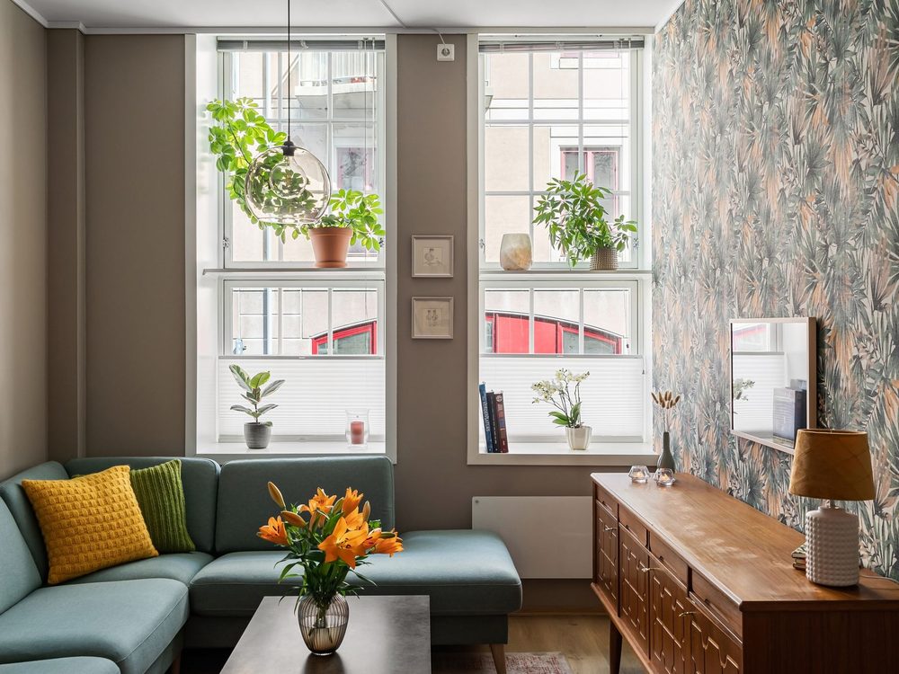 Living room with a botanical feature wall, teal sofa, and natural light